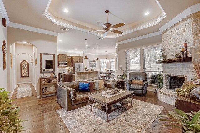 living room with hardwood / wood-style floors, ceiling fan, a raised ceiling, crown molding, and a fireplace