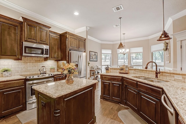 kitchen with crown molding, stainless steel appliances, a kitchen island, sink, and light hardwood / wood-style floors