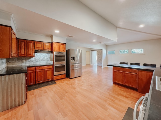 kitchen featuring appliances with stainless steel finishes, lofted ceiling, decorative backsplash, a barn door, and light hardwood / wood-style flooring