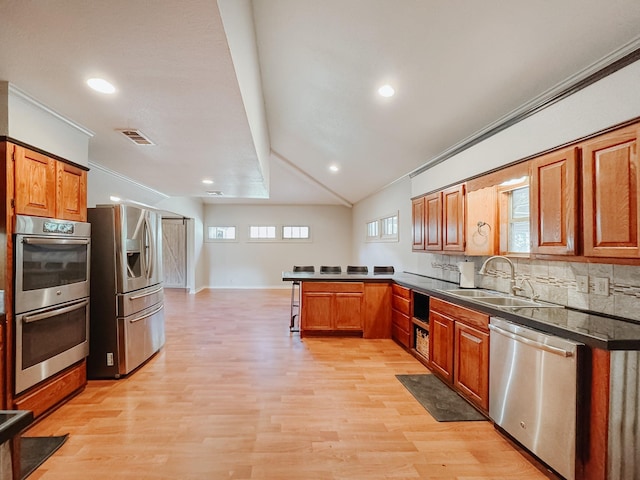 kitchen featuring sink, stainless steel appliances, backsplash, lofted ceiling, and light wood-type flooring