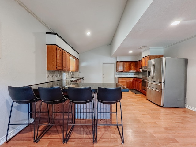 kitchen with a kitchen breakfast bar, backsplash, appliances with stainless steel finishes, and light hardwood / wood-style flooring