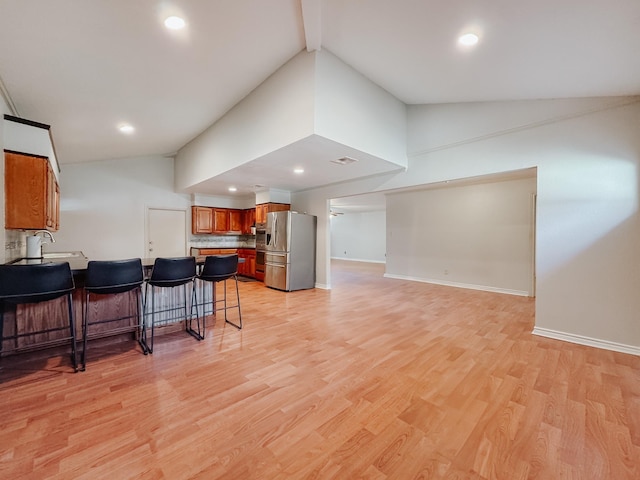 kitchen with a breakfast bar, stainless steel fridge with ice dispenser, high vaulted ceiling, and light hardwood / wood-style flooring