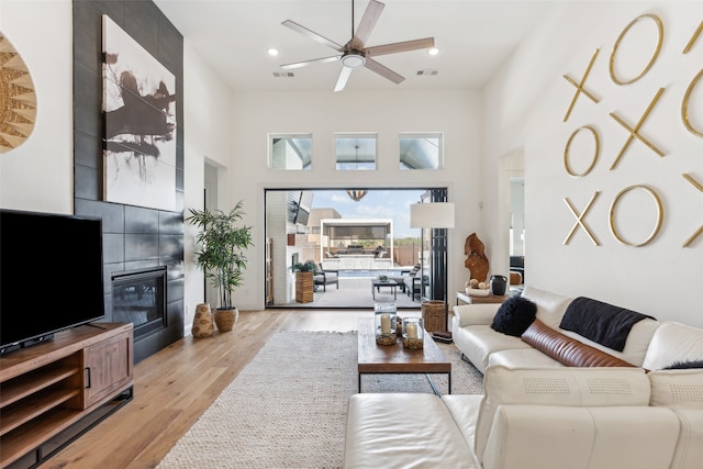 living room featuring light wood-type flooring, a towering ceiling, and ceiling fan