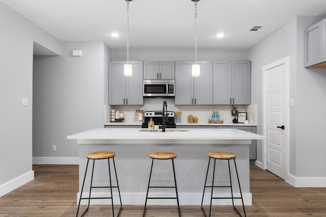 kitchen featuring appliances with stainless steel finishes, a center island with sink, and dark wood-type flooring