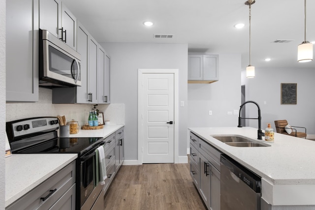 kitchen with gray cabinets, appliances with stainless steel finishes, light hardwood / wood-style flooring, sink, and decorative light fixtures