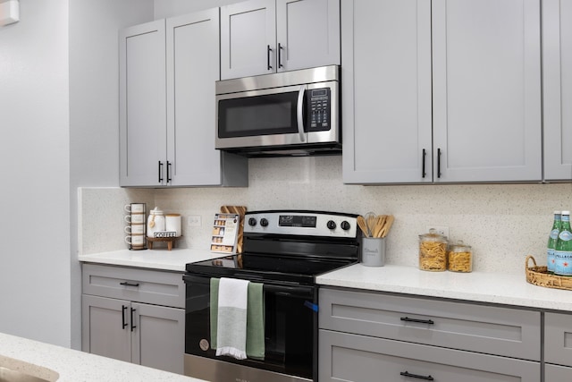 kitchen featuring appliances with stainless steel finishes, light stone counters, and gray cabinetry