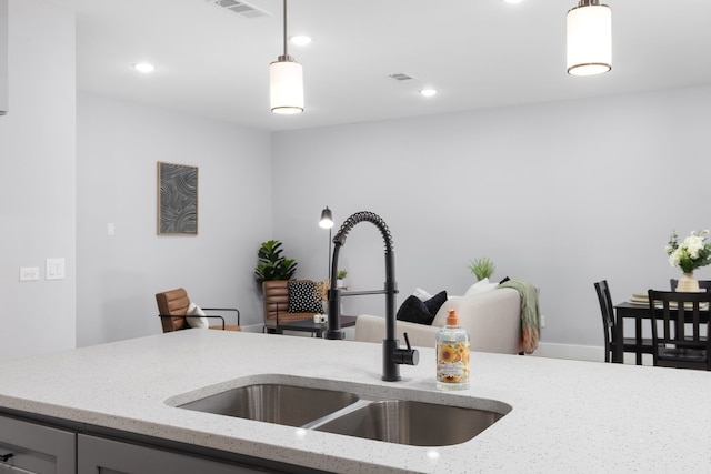 kitchen featuring light stone counters, sink, and hanging light fixtures