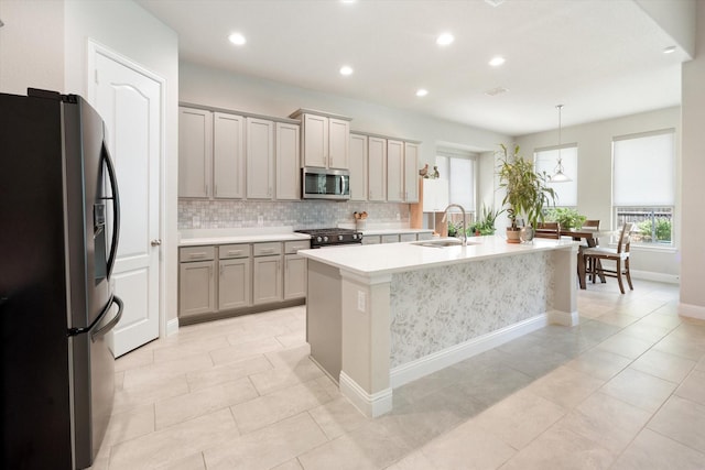 kitchen with sink, hanging light fixtures, stainless steel appliances, gray cabinets, and a center island with sink