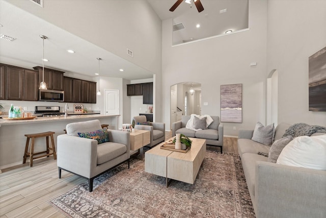 living room with light hardwood / wood-style floors, ceiling fan, and a high ceiling