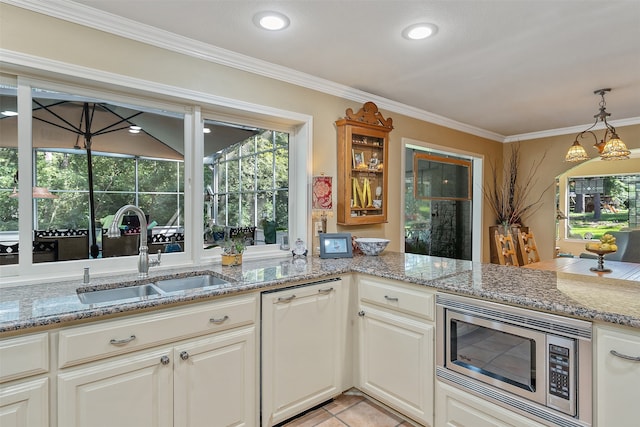 kitchen featuring stainless steel microwave, crown molding, hanging light fixtures, light stone counters, and sink