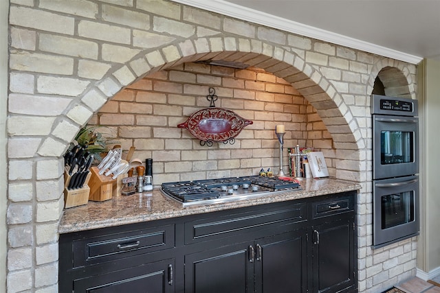 kitchen with light stone countertops, crown molding, stainless steel appliances, and brick wall