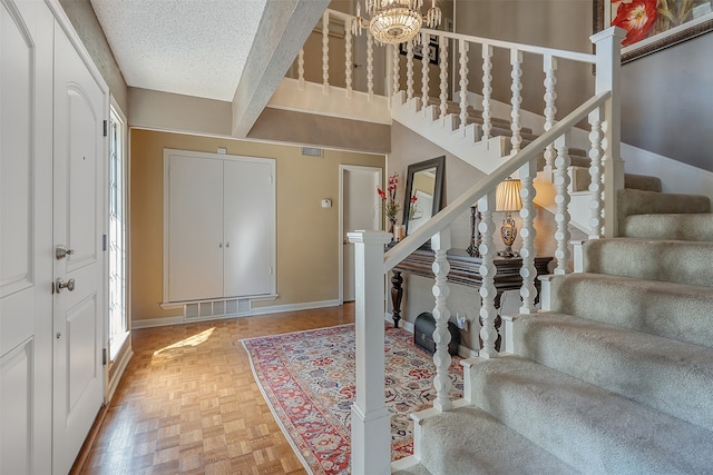 entrance foyer featuring beamed ceiling, parquet flooring, a textured ceiling, and an inviting chandelier