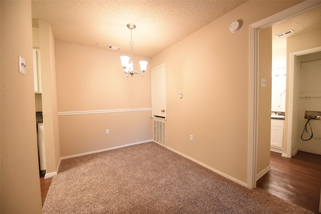 carpeted spare room with a notable chandelier and a textured ceiling