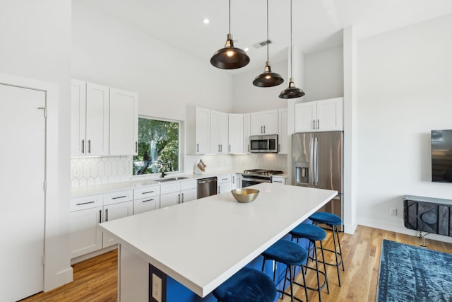 kitchen with backsplash, stainless steel appliances, light hardwood / wood-style flooring, and a high ceiling