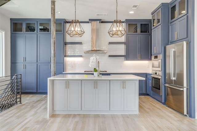 kitchen featuring decorative backsplash, a kitchen island with sink, wall chimney range hood, stainless steel appliances, and blue cabinetry