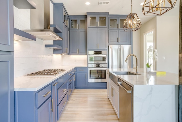 kitchen with light wood-type flooring, stainless steel appliances, hanging light fixtures, backsplash, and wall chimney range hood