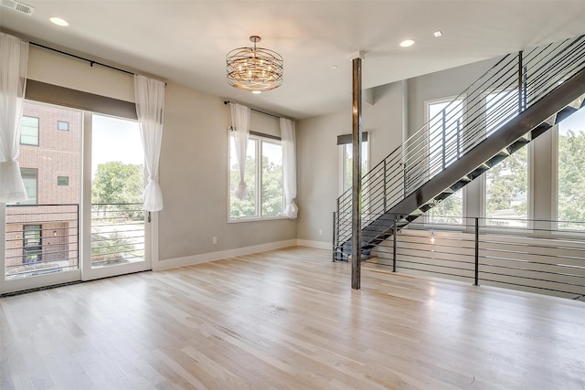 unfurnished living room featuring an inviting chandelier and light hardwood / wood-style floors