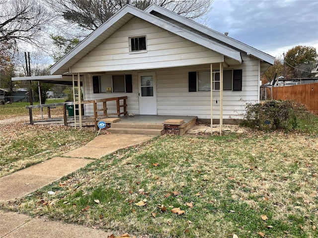 bungalow-style home with covered porch, fence, and a front lawn