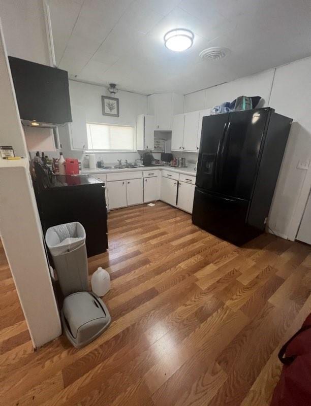 kitchen featuring light wood-style flooring, light countertops, white cabinets, black refrigerator with ice dispenser, and a sink