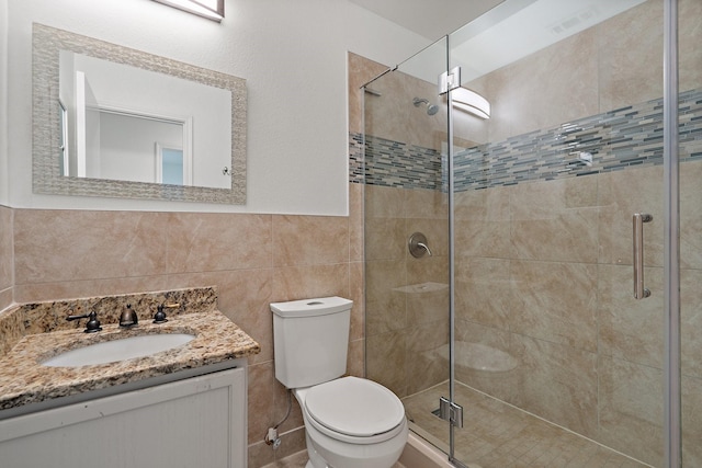 bathroom with vanity, toilet, a shower with shower door, and tile walls