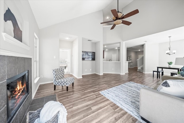 living room featuring ceiling fan with notable chandelier, high vaulted ceiling, wood-type flooring, and a tile fireplace