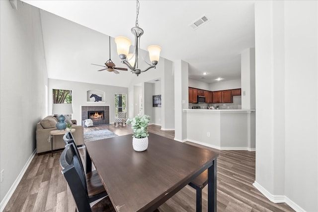 dining area featuring a fireplace, light wood-type flooring, ceiling fan with notable chandelier, and lofted ceiling