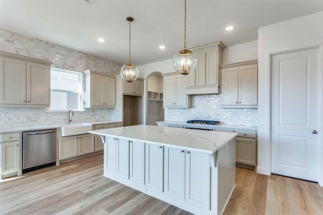 kitchen featuring arched walkways, light wood-style floors, a kitchen island, a sink, and dishwasher