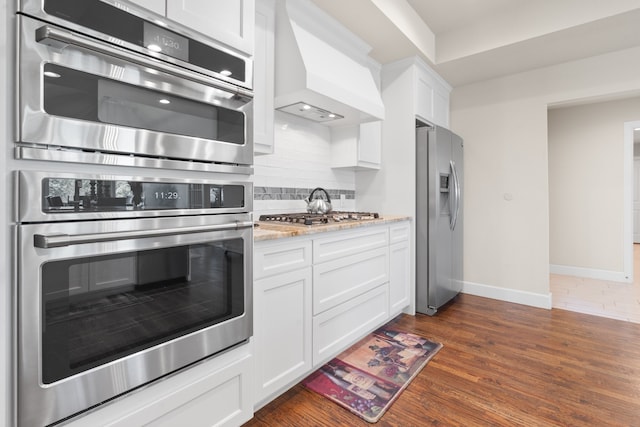 kitchen featuring custom exhaust hood, dark hardwood / wood-style floors, stainless steel appliances, white cabinets, and tasteful backsplash