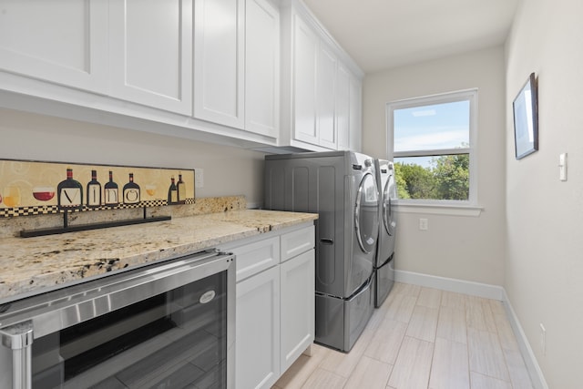 clothes washing area featuring washer and clothes dryer, cabinets, and beverage cooler