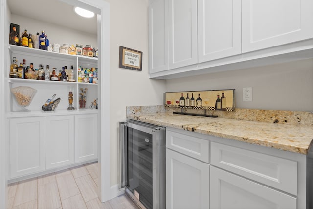 bar featuring light stone counters, beverage cooler, and white cabinetry