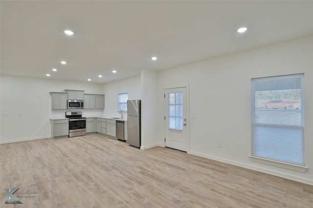 kitchen featuring appliances with stainless steel finishes, a healthy amount of sunlight, light hardwood / wood-style floors, and gray cabinetry