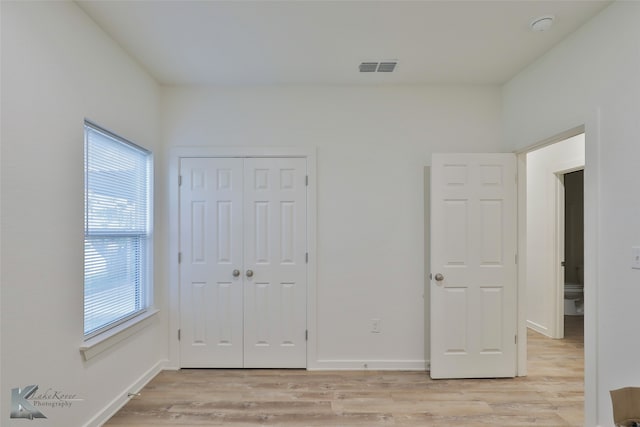 unfurnished bedroom featuring multiple windows, light hardwood / wood-style flooring, and a closet