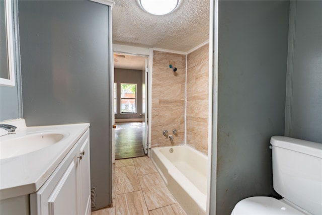 full bathroom featuring a textured ceiling, tiled shower / bath, vanity, and toilet