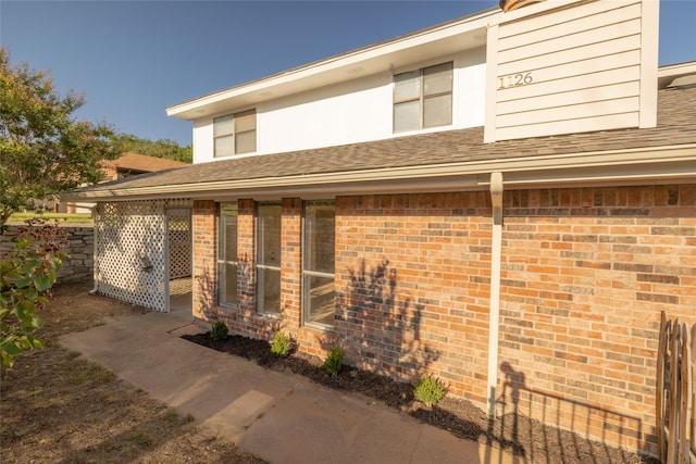 exterior space featuring brick siding and a shingled roof