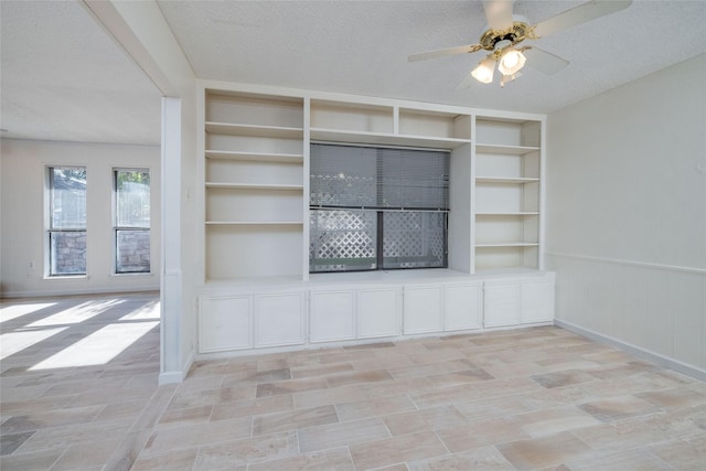 room details featuring a textured ceiling, ceiling fan, built in shelves, and a wainscoted wall