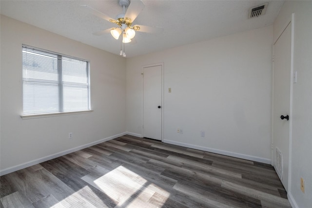 spare room featuring dark wood-style flooring, visible vents, and baseboards