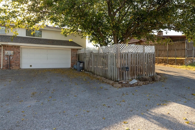 view of property exterior with a garage, driveway, brick siding, and fence