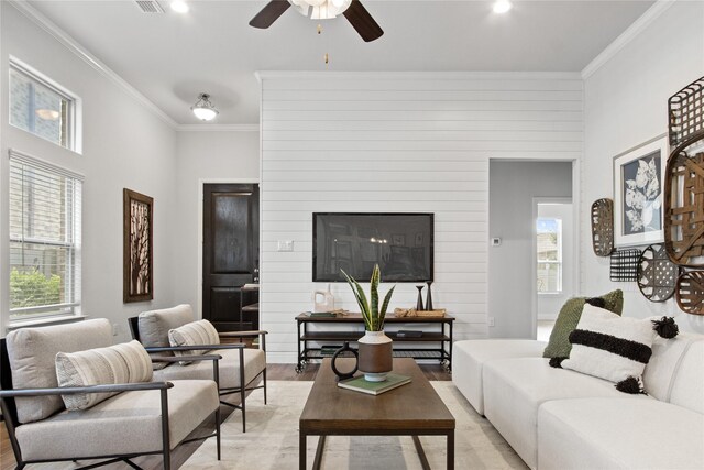 living room featuring light wood-type flooring, ornamental molding, ceiling fan, and a healthy amount of sunlight