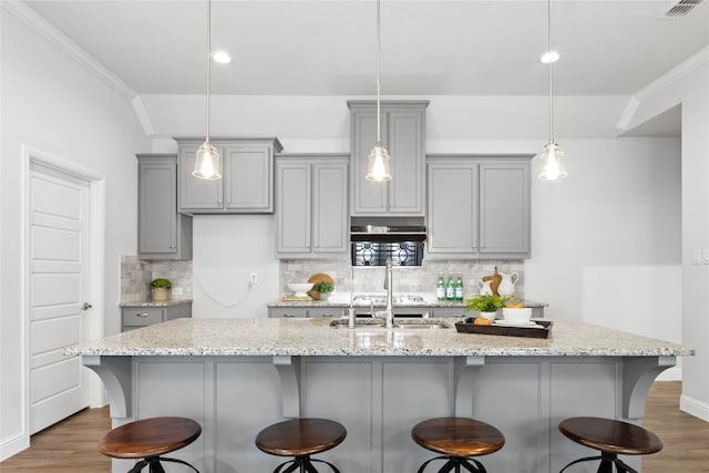 kitchen featuring hardwood / wood-style floors, backsplash, ornamental molding, and a kitchen island with sink