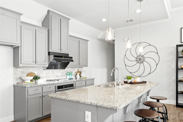 kitchen featuring hanging light fixtures, an island with sink, wood-type flooring, sink, and tasteful backsplash