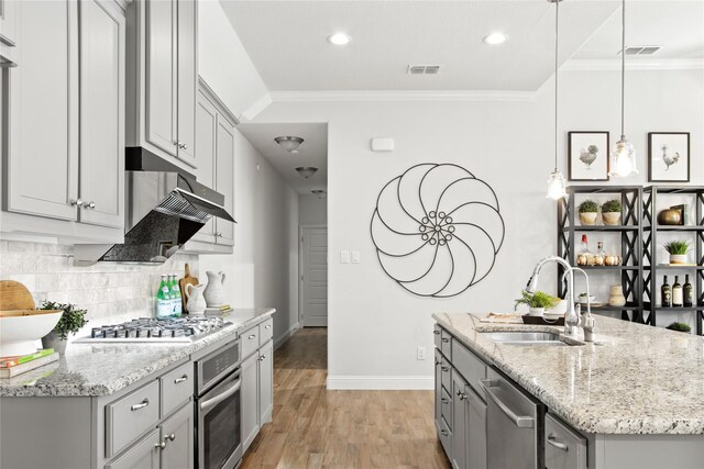 kitchen with light wood-type flooring, crown molding, appliances with stainless steel finishes, sink, and decorative light fixtures