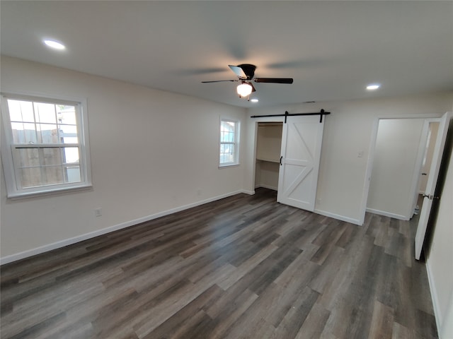 unfurnished bedroom with ceiling fan, a barn door, and wood-type flooring