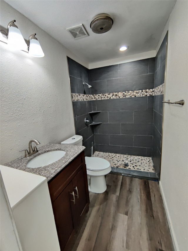 bathroom with tiled shower, hardwood / wood-style floors, toilet, and vanity