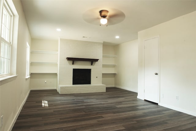 unfurnished living room featuring ceiling fan, dark wood-type flooring, brick wall, and a brick fireplace