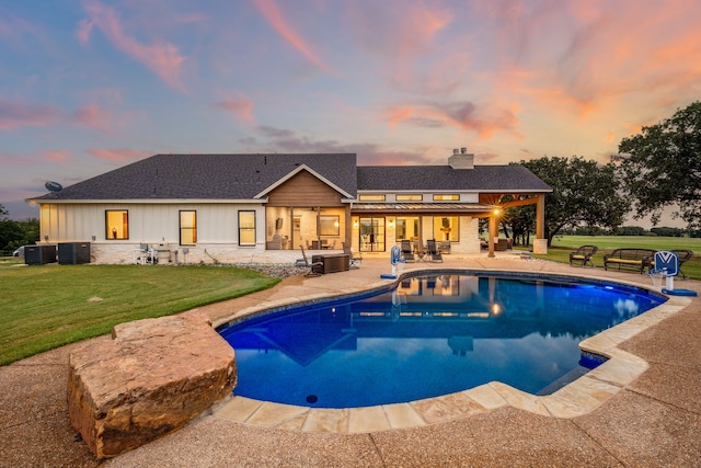 pool at dusk featuring central AC unit, a lawn, and a patio