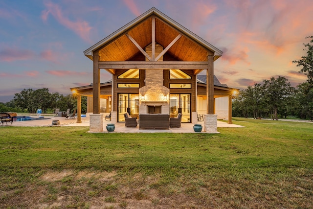 back house at dusk with a yard, an outdoor living space with a fireplace, and a patio area