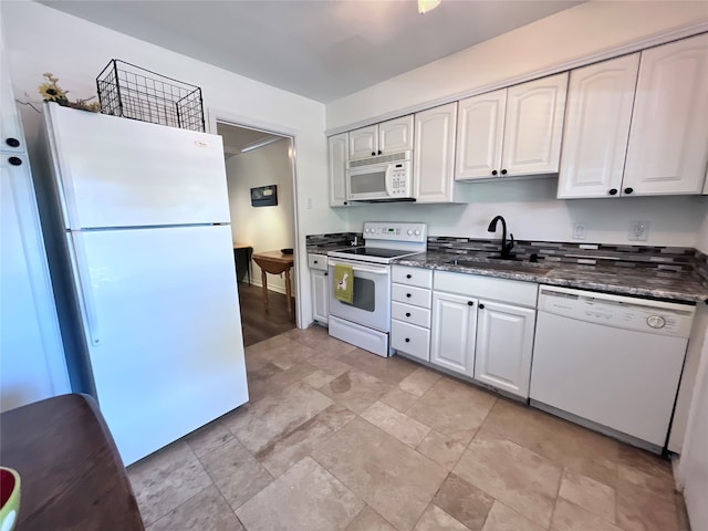 kitchen with dark stone counters, white cabinetry, white appliances, and sink