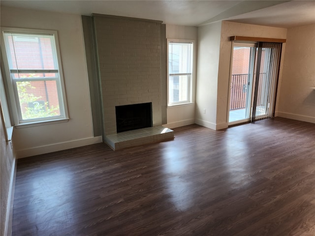 unfurnished living room featuring dark wood-type flooring, brick wall, and a brick fireplace