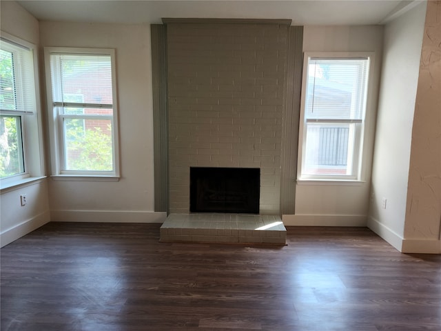 unfurnished living room featuring dark wood-type flooring and a brick fireplace