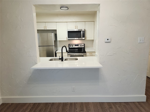 kitchen with appliances with stainless steel finishes, sink, hardwood / wood-style flooring, and white cabinetry